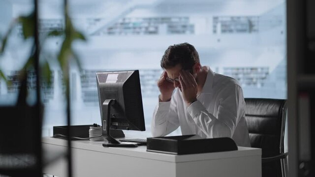 Man sit indoor closed eyes rub temples suffering from headache. Stressed young man in glasses suffering from muscles tension, having painful head feelings due to computer overwork or sedentary working