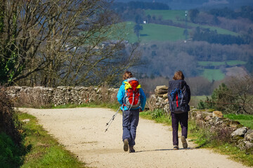 Fototapeta premium Two Pilgrim Hikers Walking on Road across Idyllic Galicia Countryside along the Way of St James Pilgrimage Trail Camino de Santiago