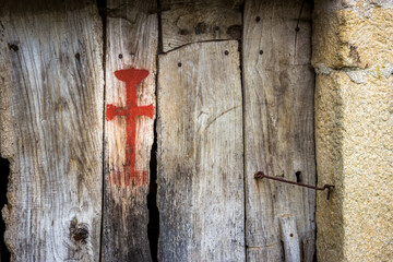 Old Ancient Wooden Door with Red Pilgrim Santiago Cross along the Way of St James Pilgrimage Trail Camino de Santiago