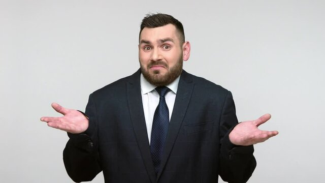 Unhappy bearded businessman in black official style suit looking at camera, clenching teeth expressing hate, annoyance. Indoor studio shot isolated on gray background.