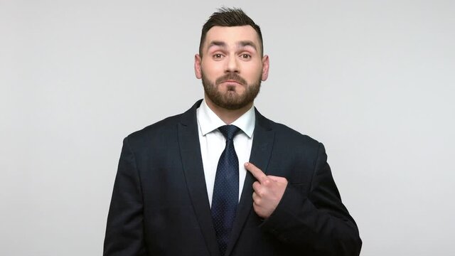Proud satisfied bearded businessman in black official style suit smiling satisfied and pointing himself, feeling self-important, famous. Indoor studio shot isolated on gray background.