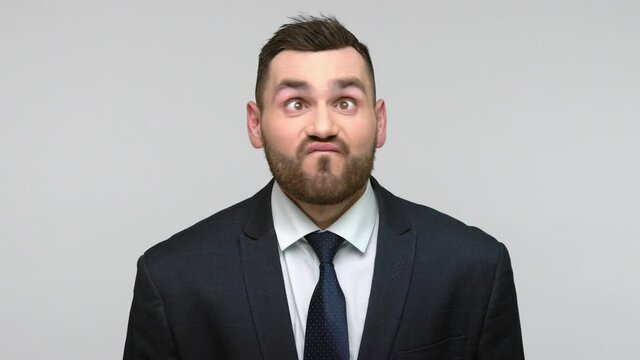 Stupid funny bearded businessman in black official style suit looking with crossed eyes, grimacing, making silly brainless dumb face. Indoor studio shot isolated on gray background.