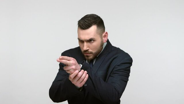 Dangerous self confident criminal bearded businessman in suit threatening with finger pistols, shooting to camera, gesturing weapon and killing. Indoor studio shot isolated on gray background.