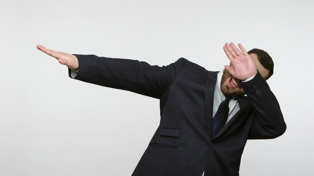 Bearded businessman in black official style suit celebrating success with dab dance move, famous internet meme of triumph, performing dabbing trends. Indoor studio shot isolated on gray background.