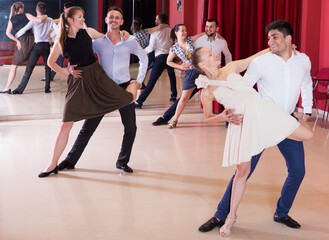 Adult dancing couples enjoying latin dances in modern studio