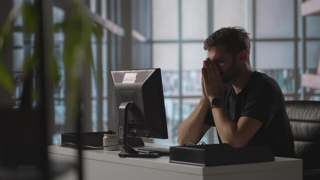 A serious man sits at a computer in the office and thinks. Analyzes solves a crisis problem. A difficult stage in business. Thoughtful businessman