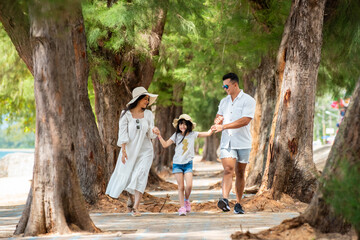Happy Asian family parent with little daughter holding hand and walking together by the beach in summer day. Father and mother with cute child girl kid enjoy outdoor lifestyle activity on vacation.
