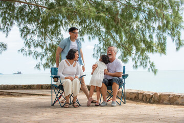 Happy multi generation Asian family enjoy picnic travel together on the beach in summer. Parents with retired senior grandparent and cute child girl relax and having fun on summer holiday vacation