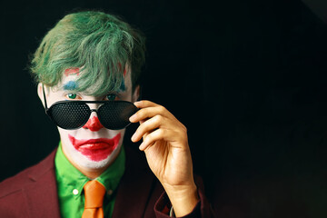 Man in mime makeup cosplay with green hair and a red suit an orange tie and a green shirt. Clown...
