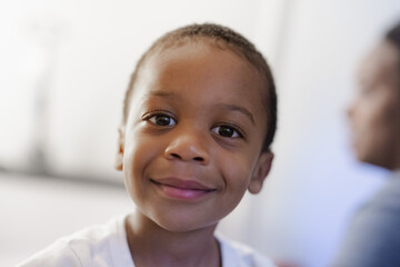 Young Black boy toddler smiling with mother in background, blurred, handsome