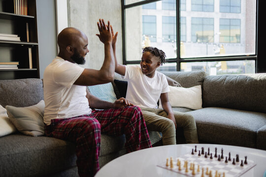 Black Father and son sitting on sofa in living room, giving high five