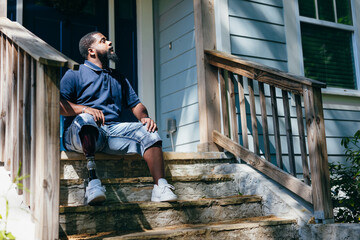 Black man with prosthetic leg sitting at front porch of new home purchase