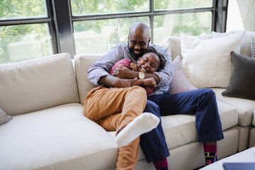 Playful Black father and son sitting on sofa