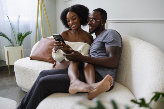 Smiling couple sitting on sofa and using smart phone