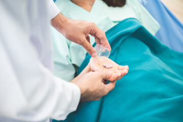 Young woman suffering with corona virus infection lying on hospital bed with mask sleeping and resting while doctor taking notes of progress and writing on clipboard in background wearing ppe kit