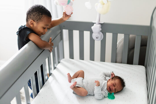 Big brother checking on sibling in crib, crying baby