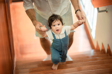 Fototapeta premium Cute little playful girl child learning to walk and stand by taking support of couch at home while looking away mischievously