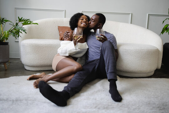 Smiling couple cuddling and drinking white wine in living room