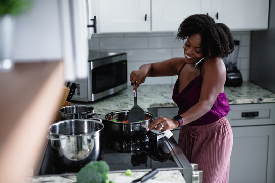 Black woman cooking at talking on phone, multitasking 