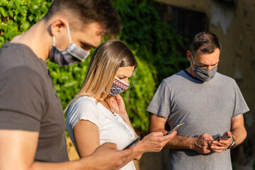Group of friends in summer vacation after lockdown using mobile phone app - Tourists checking map on the smartphone while wearing protective masks - millennial new normal lifestyle friendship concept