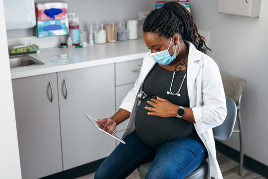 Black pregnant doctor reviewing medical records on tablet