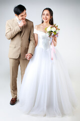Full length of young attractive Asian couple, man wearing beige suit, woman wearing white wedding gown standing together holding hands. Concept for pre wedding photography