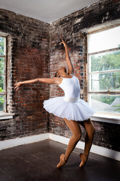 Fototapeta Black ballerina doing powerful ballet dance pose, wearing pointe shoes and white tutu, perseverance 