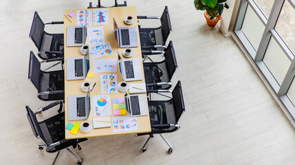 Top view shot of conference meeting room in company office full of laptop notebook computers on working desk with black chairs and big screen monitor and glass board with post it data paper documents