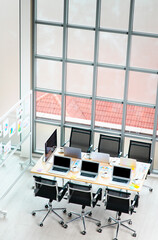 Top view shot of conference meeting room table in empty company office full of laptop computers coffee cups report data paperwork documents black chairs and glass board near building glass windows