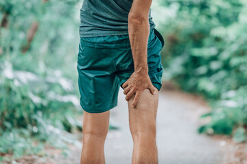 Leg muscle pain sports injury runner man touching painful hamstring muscle. Legs physiotherapy care athlete massaging sore muscles during running training in summer park outside. - obrazy, fototapety, plakaty
