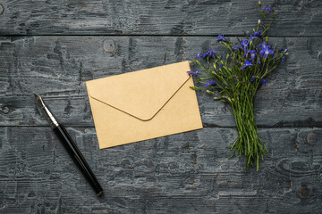 A fountain pen, a paper postal envelope and a bouquet of flowers on a wooden table. Flat lay.