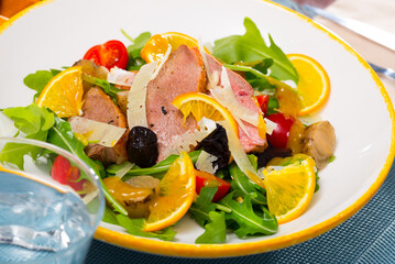 Colorful salad from duck fillets with fresh arugula, tomatoes, fried onions, sliced parmesan cheese, prunes and orange..