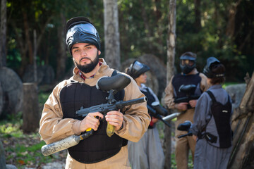 Fototapeta premium Man and his paintball sport team in protective uniform at paintball shooting range