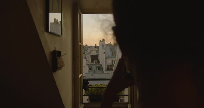 A Silhouetted Person From Behind Taking Photos with a Mobile Phone Looking Out Over Rooftops in Paris, France.