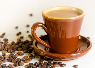 Old rare Scandinavian cup brown color of baked clay with coffee and milk in a saucer placed on a table on which coffee beans are scattered Arabica