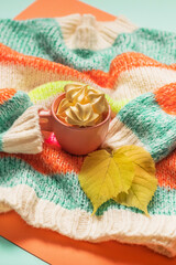 Obraz na płótnie Canvas Airy pink marshmallows in a cup on a knitted multicolored sweater with autumn leaves. Rainbow colors, copy space.