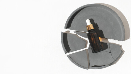 cosmetic oil or serum in amber glass bottle with dropper. golden lid decor. a bottle on broken cement tray on white background. copy space.