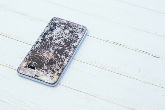 Broken glass screen smartphone on a light-colored wooden floor. Leave the copy space.