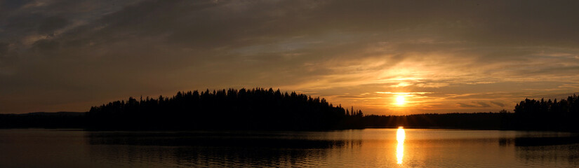Panorama summer sunset with the reflection of the sun in the lake.