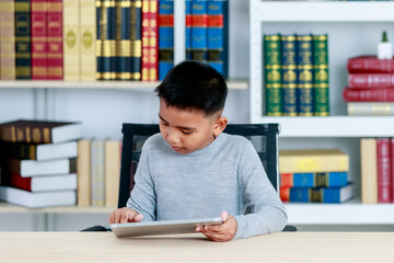 Asian boy on grey sweatshirt sit at school desk, lower head down to concentrate on online class...