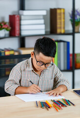 Smart Asian boy wearing glasses and grey checked shirt sitting on studying desk of tablet, mobile...