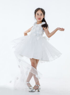 Portrait isolated studio shot of little Asian cute ballerina kid in pink beautiful ballet dress with high heels standing smiling posing elegance gesture in front white background