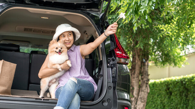  Asia women hugging her lovely puppy pomeranian dog at the back of suv car on travel tip and copy space