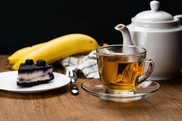 View of hot tea in transparent cup and slice of blueberry cheesecake in white ceramic dish for...