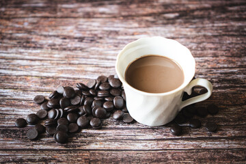 Portion of homemade hot cocoa in a cup with dark chocolate chips on a wooden background.