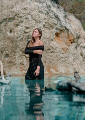 Blue Lagoon. A girl in a black dress stands in bright blue water. Lake, rates. Dead tree in the water.