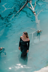 Blue Lagoon. A girl in a black dress stands in bright blue water. Lake, rates. Dead tree in the water.