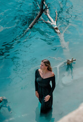 Blue Lagoon. A girl in a black dress stands in bright blue water. Lake, rates. Dead tree in the water.