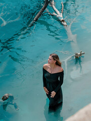 Blue Lagoon. A girl in a black dress stands in bright blue water. Lake, rates. Dead tree in the water.