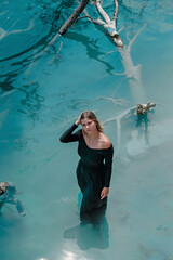 Blue Lagoon. A girl in a black dress stands in bright blue water. Lake, rates. Dead tree in the water.